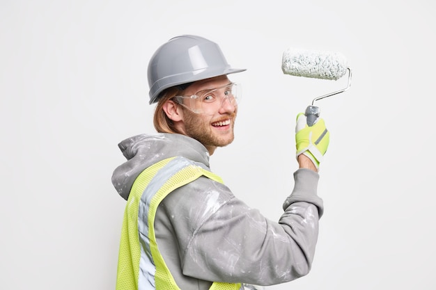 Foto grátis homem pinta uma nova casa segura rolo usa capacete de proteção e uniforme repara poses em branco