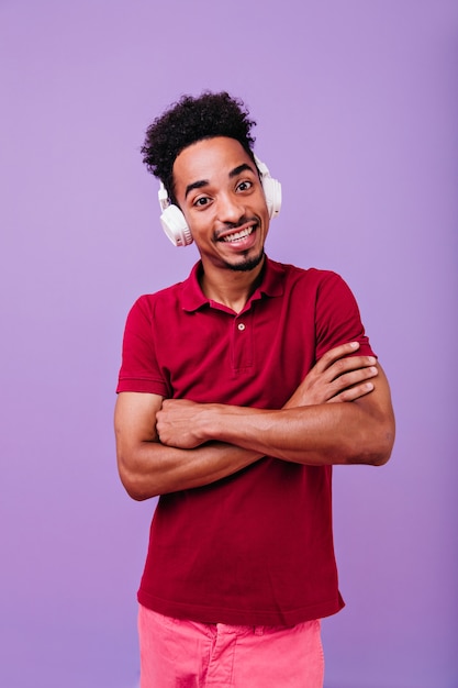 Homem positivo com grandes olhos castanhos olhando com os braços cruzados. menino alegre moreno em fones de ouvido.