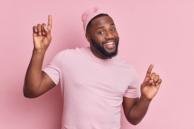 Homem positivo de pele escura com barba espessa dança despreocupado, levanta os braços, tem bom humor