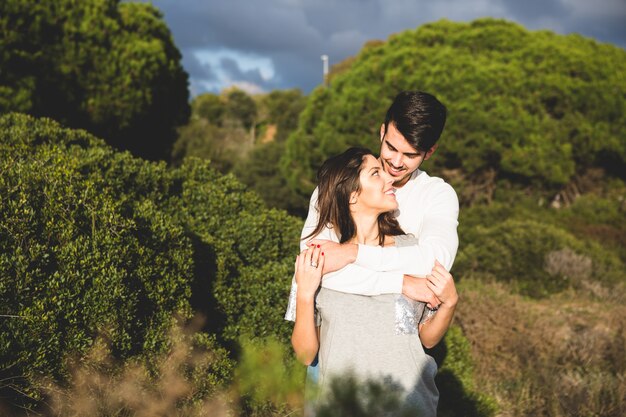 Homem que abraça mulher por trás com uma floresta com árvores atrás