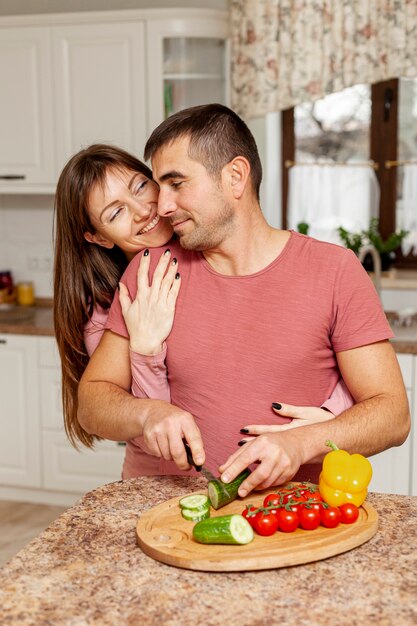 Homem que corta vegetais abraçados por sua namorada