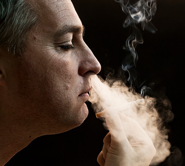 Foto grátis homem que fuma cigarro no fundo preto, homem novo bonito que fuma cigarro, homem misterioso com charuto e fumo isolado no fundo preto