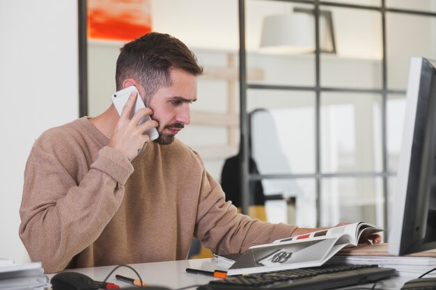 Homem que lê a revista e fala no smartphone