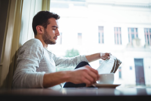 Homem que tem uma chávena de café ao ler o jornal