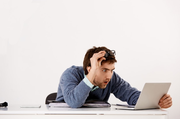 Foto grátis homem que trabalha no escritório, decolar óculos e olhando confuso com a tela do laptop descrença, lendo notícias chocantes, receber curioso relatório