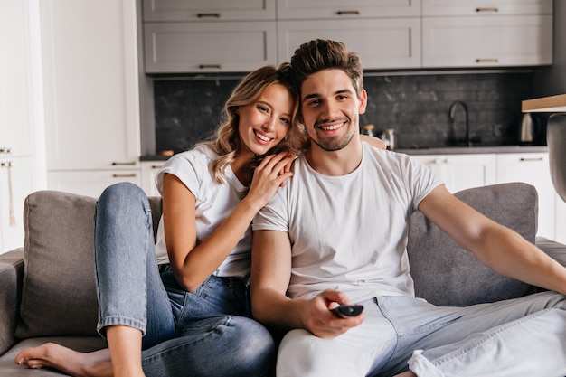 Homem relaxado assistindo TV. Menina loira graciosa sentada no sofá com o marido.