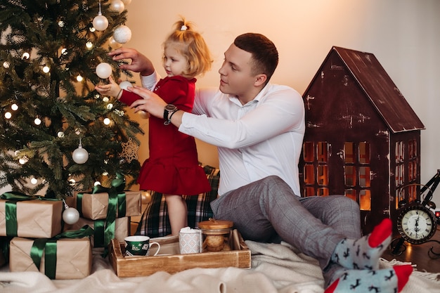 Homem responsável ajudando criança fofa a colocar enfeites na árvore de Natal