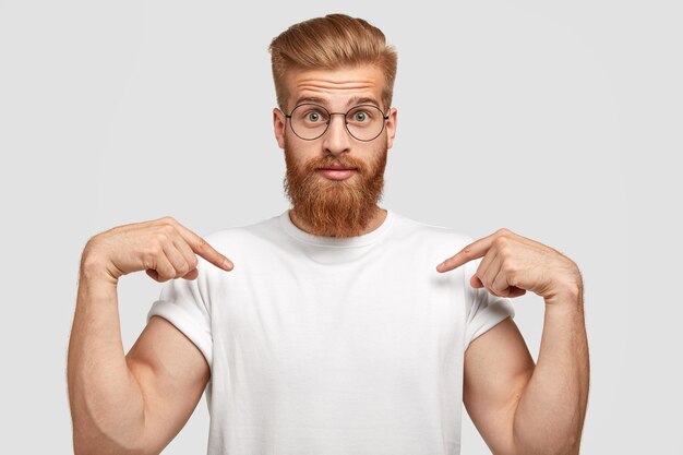 Homem ruivo estupefato tem barba espessa, aponta para o espaço da cópia da camiseta, mostra lugar para slogan ou logotipo