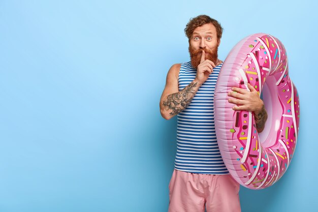 Homem ruivo satisfeito posando com piscina de donut flutuante