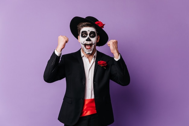 Homem satisfeito com a maquiagem assustadora mexicana, expressando felicidade. foto de estúdio de feliz modelo masculino jovem comemorando o dia dos mortos.