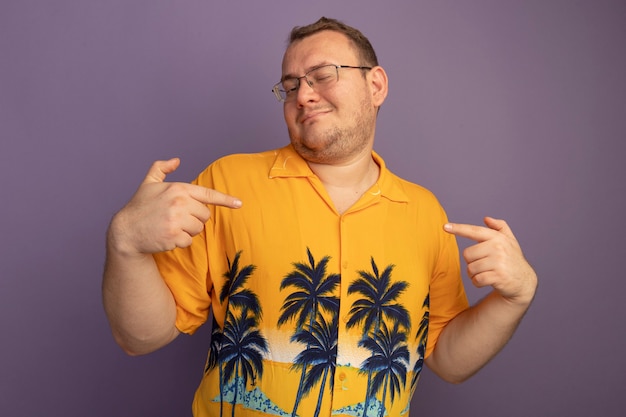 Foto grátis homem satisfeito de óculos com camisa laranja apontando para si mesmo, feliz e alegre em pé sobre a parede roxa