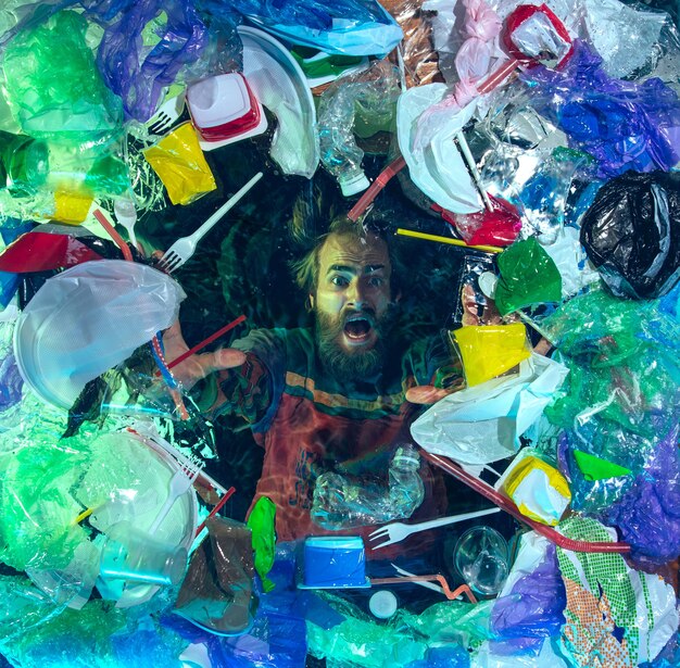 Homem se afogando em água sob a pilha de recipientes de plástico, lixo. Ecologia, conceito de meio ambiente