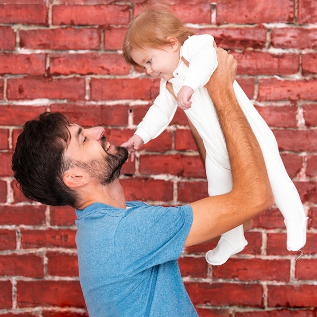 Foto grátis homem segurando bebê com fundo de tijolo