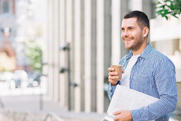 Homem segurando jornal e café perto do prédio