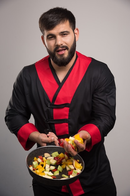 Homem segurando legumes na panela escura.