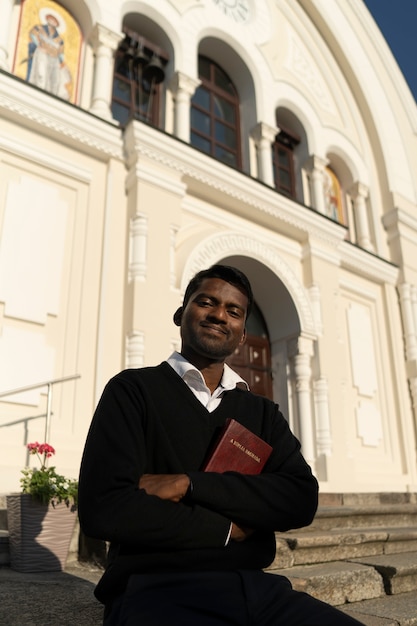 Homem segurando livro bíblico fora da igreja