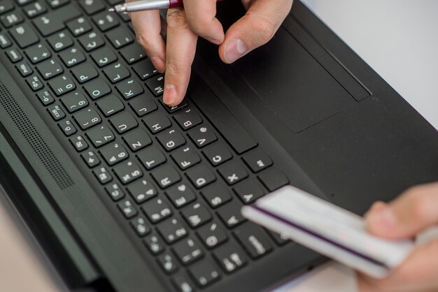 Homem segurando o cartão de crédito na mão e inserindo o código de segurança usando o telefone inteligente no teclado do laptop, conceito de compras on-line.