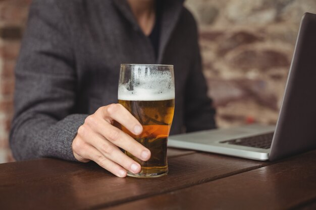 Homem segurando o copo de cerveja e usando o laptop