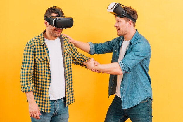 Foto grátis homem segurando seu amigo usando óculos de realidade virtual em fundo amarelo