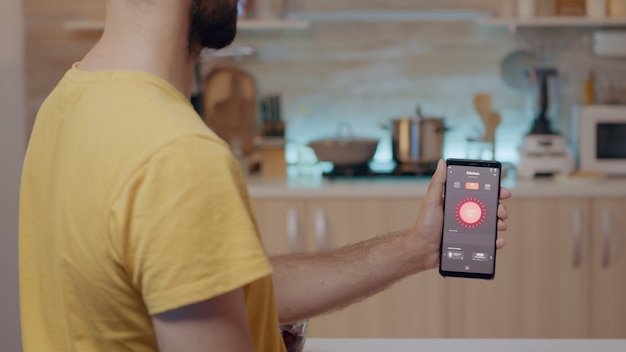 Homem segurando um celular com app de controle de iluminação sentado na cozinha