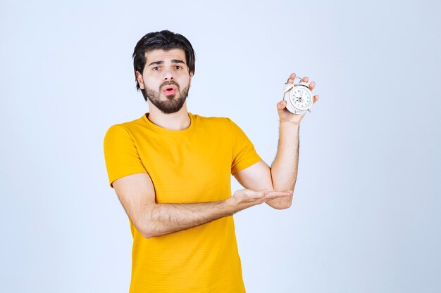 Homem segurando um despertador e parece espantado.