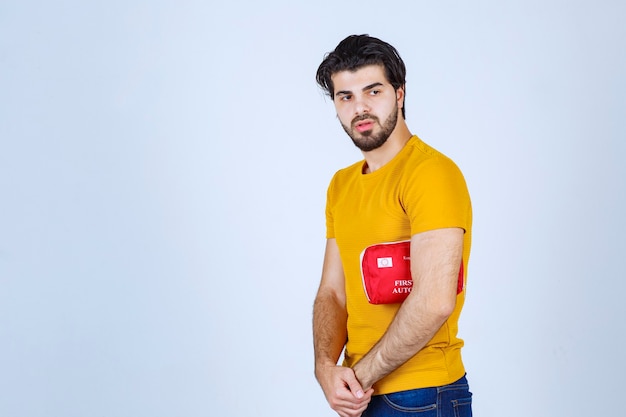 Homem segurando um kit vermelho de primeiros socorros debaixo do braço.