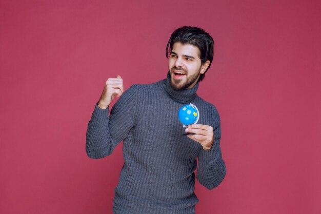 Homem segurando um mini globo azul e demonstrando-o para a multidão.