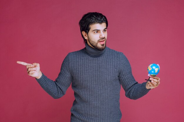 Homem segurando um mini globo e apontando para a esquerda.