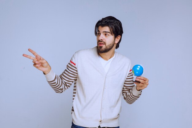 Homem segurando um mini globo e apontando para algo à esquerda.