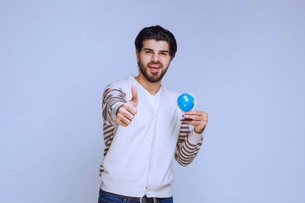 Homem segurando um mini-globo e parece que estudou todos os locais e o mapa.