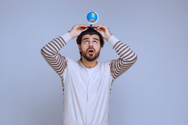 Homem segurando um mini globo sobre a cabeça.