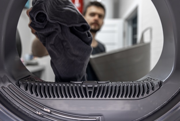 Homem segurando um pano sujo na vista de mão dentro da máquina de lavar.