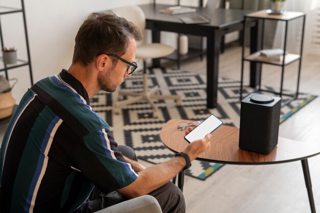Homem segurando um smartphone enquanto usa um alto-falante inteligente