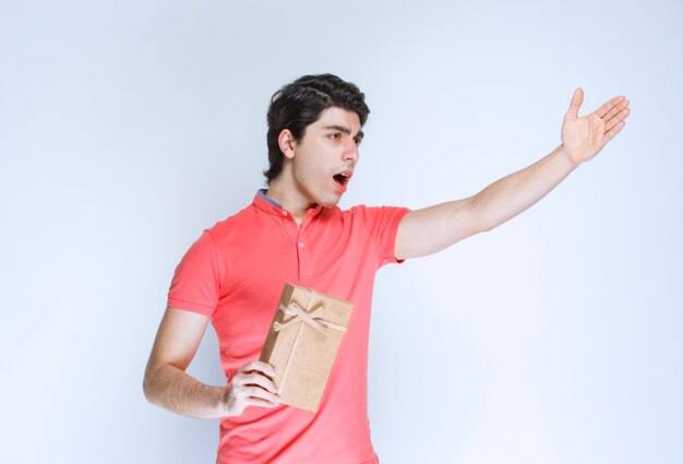 Homem segurando uma caixa de presente de papelão e apontando para algum lugar.