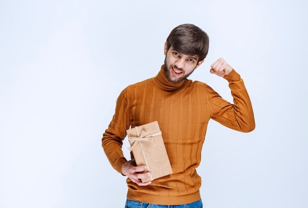 Homem segurando uma caixa de presente de papelão e mostrando sinal de prazer.