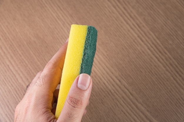 Homem segurando uma esponja de cozinha no fundo de madeira