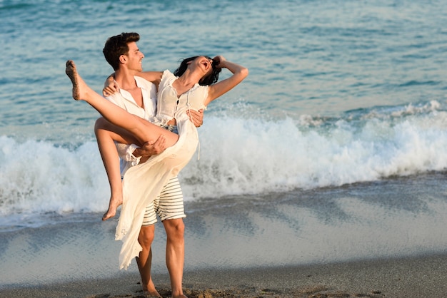 Homem segurando uma mulher no vestido branco na praia