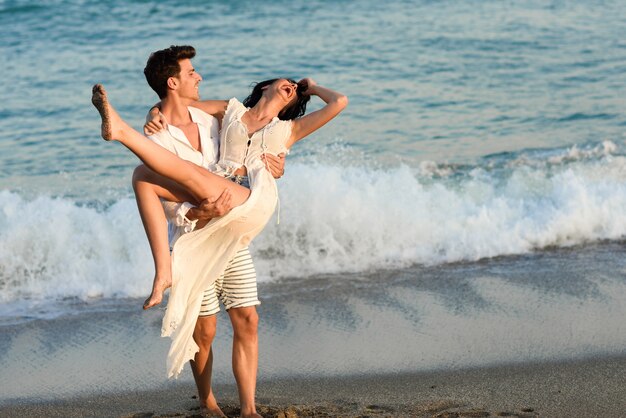 Homem segurando uma mulher no vestido branco na praia