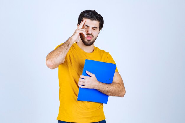 Homem segurando uma pasta azul e pensando.