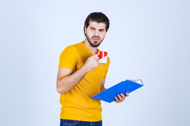 Homem segurando uma pasta azul e tomando uma xícara de café na hora do café.