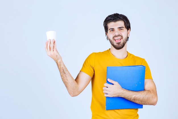 Homem segurando uma pasta azul e uma xícara de café.