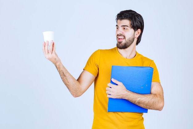 Homem segurando uma pasta azul e uma xícara de café.