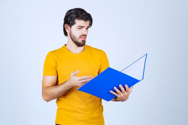 Homem segurando uma pasta azul e verificando os relatórios.