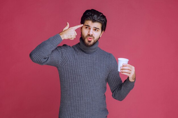 Homem segurando uma xícara de café descartável e pensando.