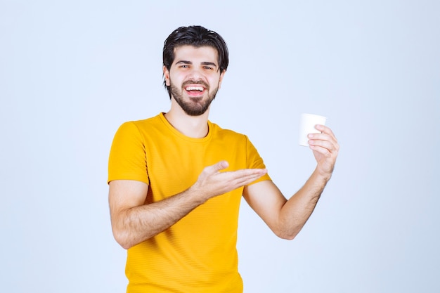 Homem segurando uma xícara de café e fazendo uma apresentação com a mão aberta.