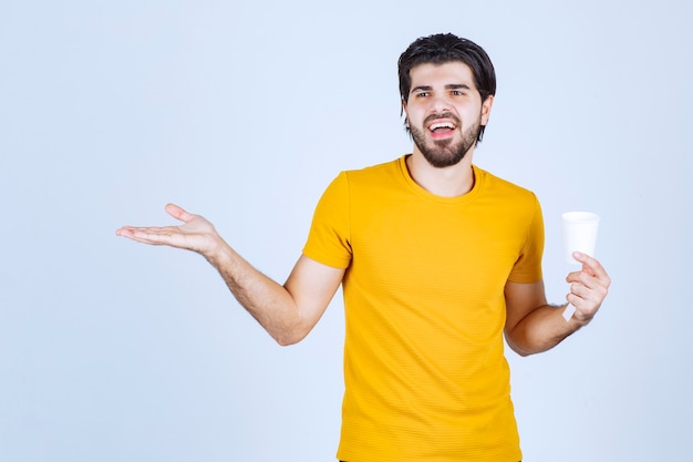 Foto grátis homem segurando uma xícara de café e fazendo uma apresentação com a mão aberta.