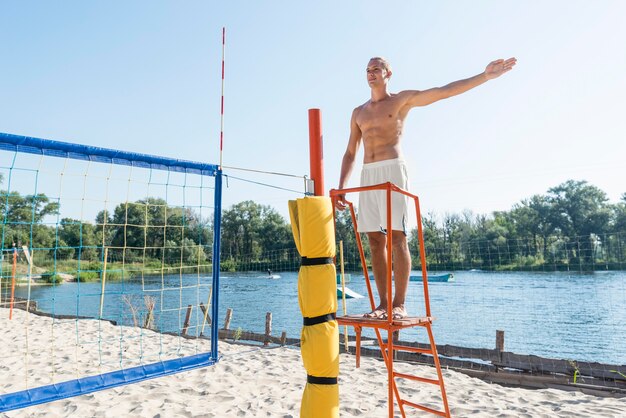 Homem sem camisa atuando como árbitro de uma partida de vôlei de praia