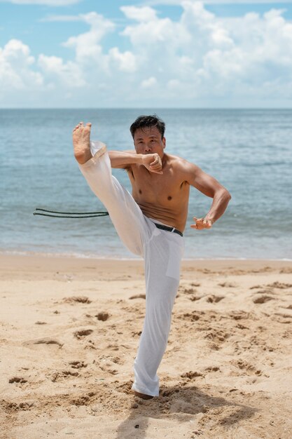 Homem sem camisa praticando capoeira na praia