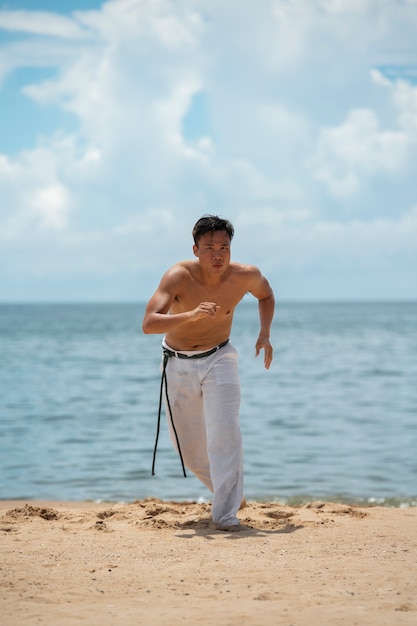 Homem sem camisa praticando capoeira sozinho na praia