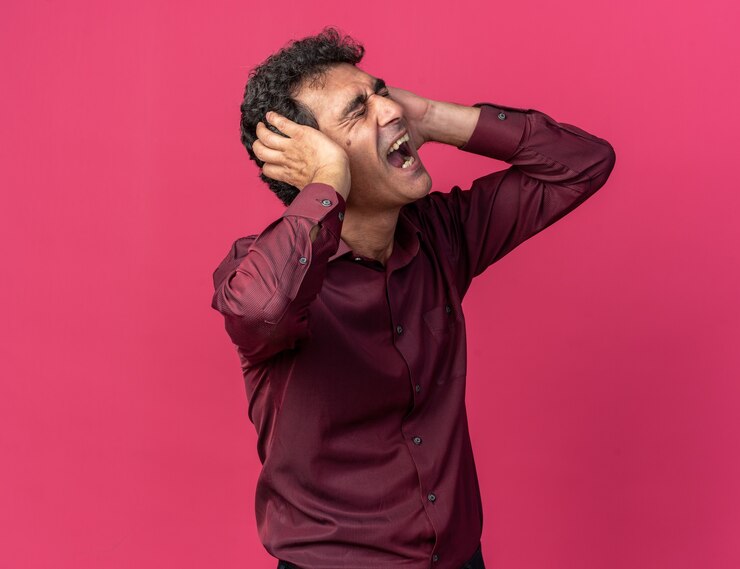 Foto grátis homem sênior com camisa roxa cobrindo as orelhas com as mãos gritando e uma expressão irritada